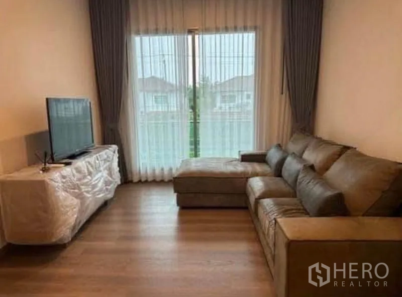 บ้าน ให้เช่า - ห้องนั่งเล่นพร้อมโซฟาเข้ามุม ตู้ทีวี และประตูกระจกเลื่อนกับผ้าโปร่ง