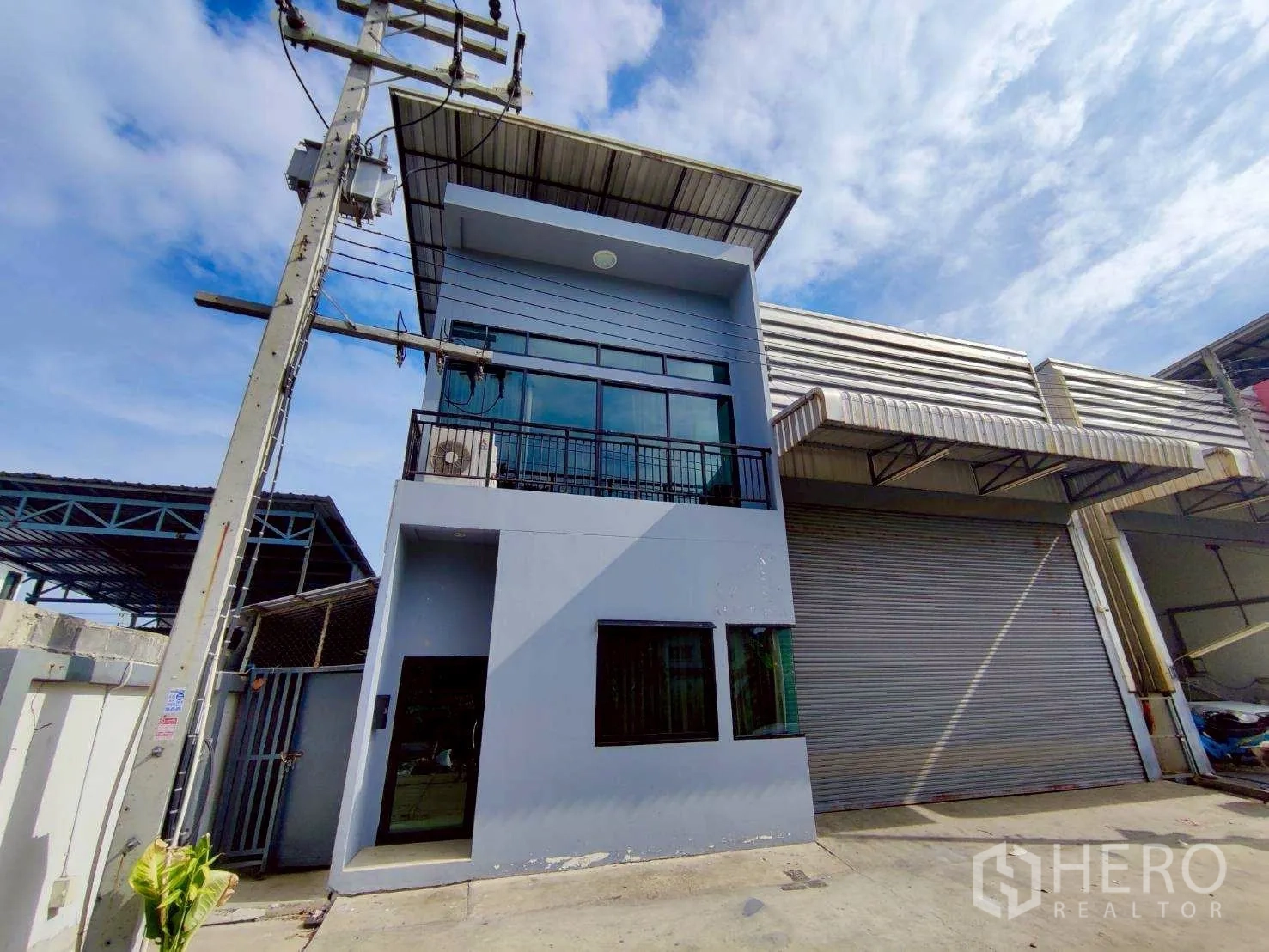 Warehouse for rent in Lam Luk Ka, Pathum Thani - Street-side view of warehouse facade with shutter door and balcony.