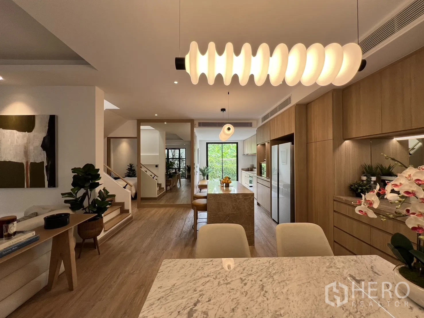 Townhouse for sale in Watthana, Bangkok - Wide view through the kitchen toward the garden with pendant lighting over the island.