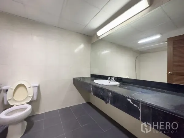 Condominium for sale in Samut Prakan - Spacious bathroom with long black marble vanity, large mirror and tiled walls.