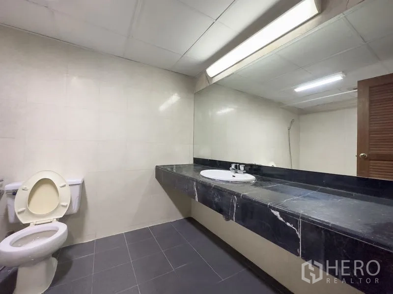 Condominium for sale in Samut Prakan - Spacious bathroom with long black marble vanity, large mirror and tiled walls.
