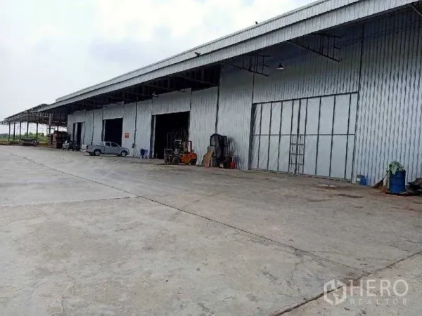 Warehouse for rent in Nong Suea, Pathum Thani - Long warehouse building with multiple loading bays, a forklift, and a wide yard for truck maneuvering.