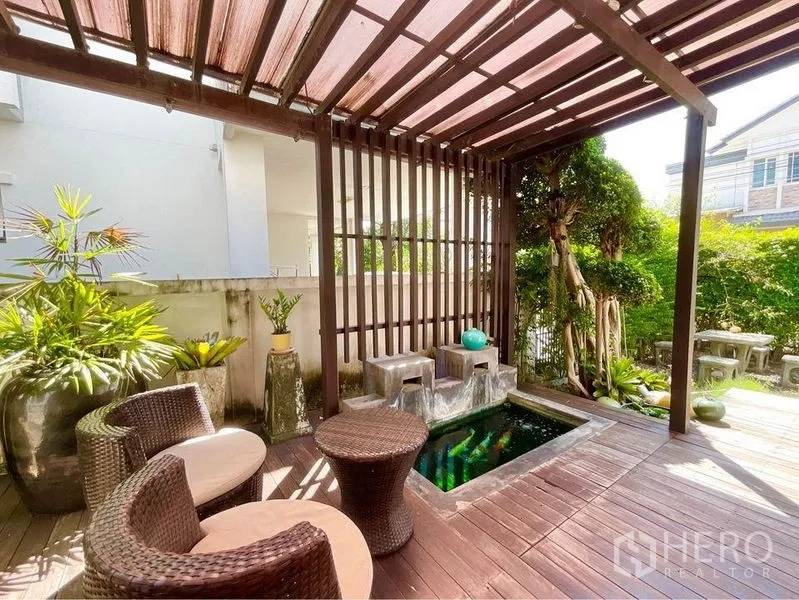 Detached House for sale in Prawet, Bangkok - Shaded wooden deck with pergola, rattan chairs and a small pond water feature in the garden.