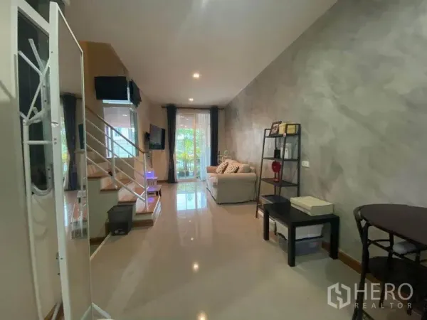 Townhouse for sale in Saphan Sung, Bangkok - Open-plan living area with glossy tiles, staircase, sofa and shelving leading to glass doors and greenery outside.