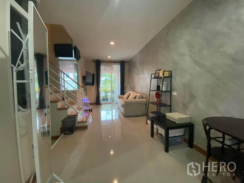 Townhouse for sale in Saphan Sung, Bangkok - Open-plan living area with glossy tiles, staircase, sofa and shelving leading to glass doors and greenery outside.