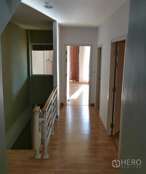 联排别墅 出租在Wang Thonglang, Bangkok - 二层走廊木地板与白色楼梯扶手，卧室门口采光充足。