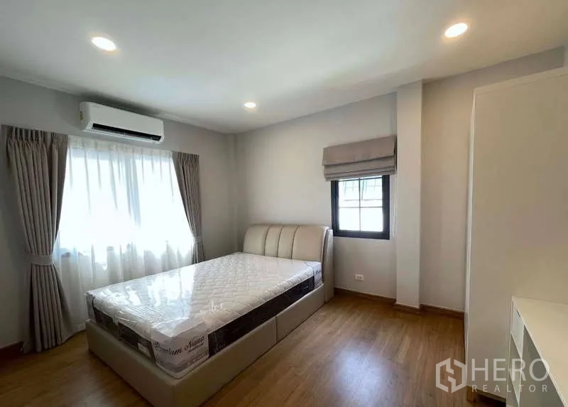 Detached House for rent in Bang Phli, Samut Prakan - Bright bedroom with air conditioner, bed and soft drapes over wood floors