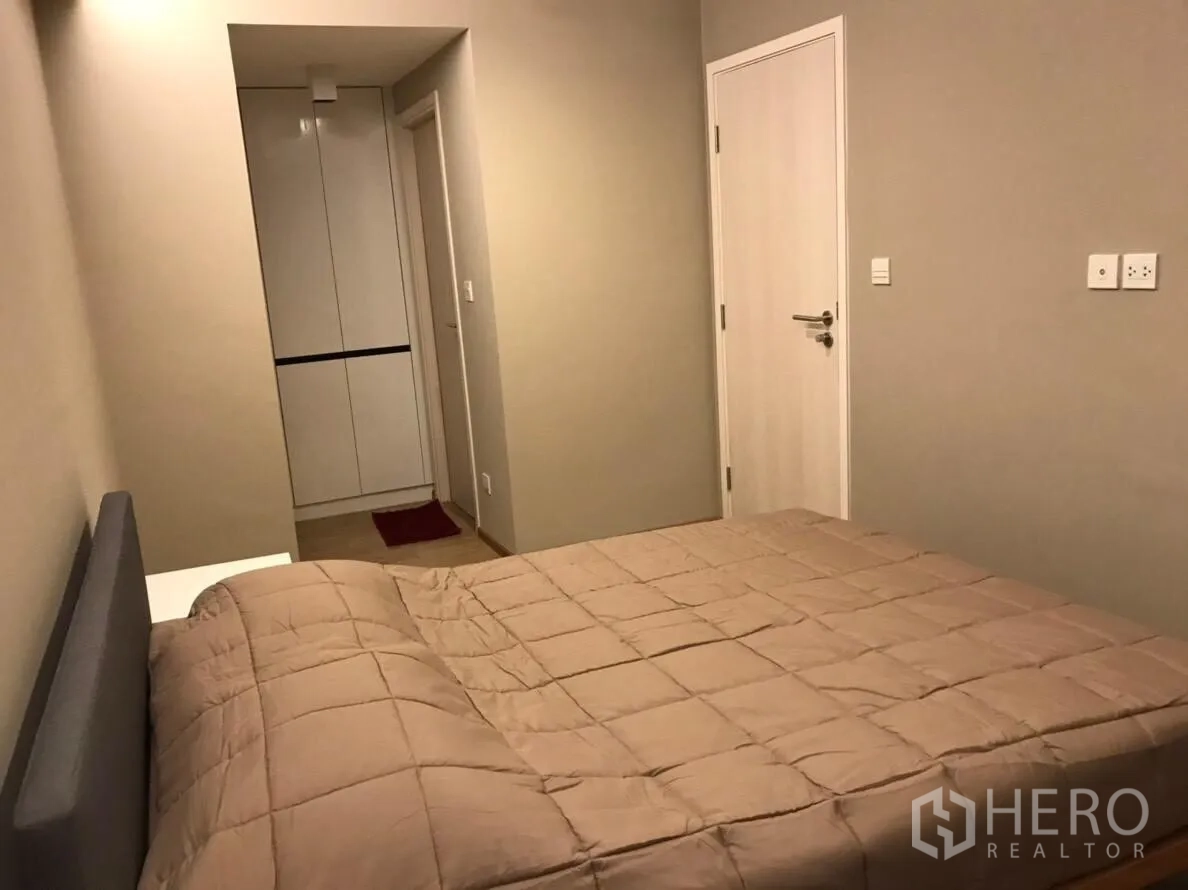 Condominium for rent in Watthana, Bangkok - Bedroom with beige bedding, built-in wardrobe and minimalist doors.