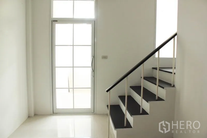 Home Office for rent in Khlong Toei, Bangkok - Minimal staircase with black treads and white railing beside a glass door and transom window.