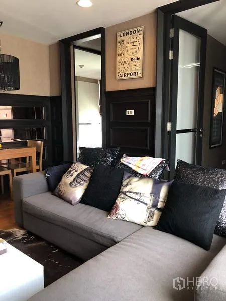 Condominium for rent in Pathum Wan, Bangkok - Living area with gray sofa, dining nook and doors leading toward the kitchen.