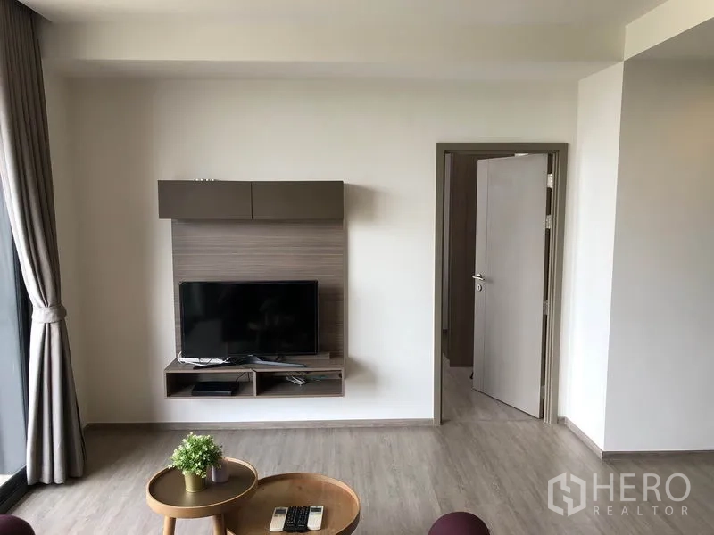 คอนโด ให้เช่าในWatthana, Bangkok - พื้นที่นั่งเล่นโมเดิร์นติดตั้งชั้นวางทีวี พื้นไม้โทนอ่อน และประตูเข้าสู่ห้องนอน