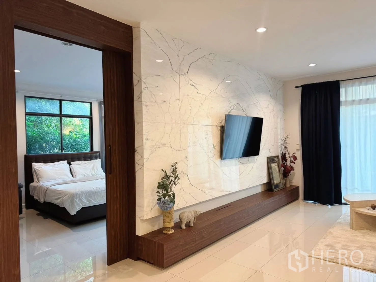 Detached House for rent or sale in Suan Luang, Bangkok - Living area with marble feature wall and TV, view into bedroom through wooden doorway.