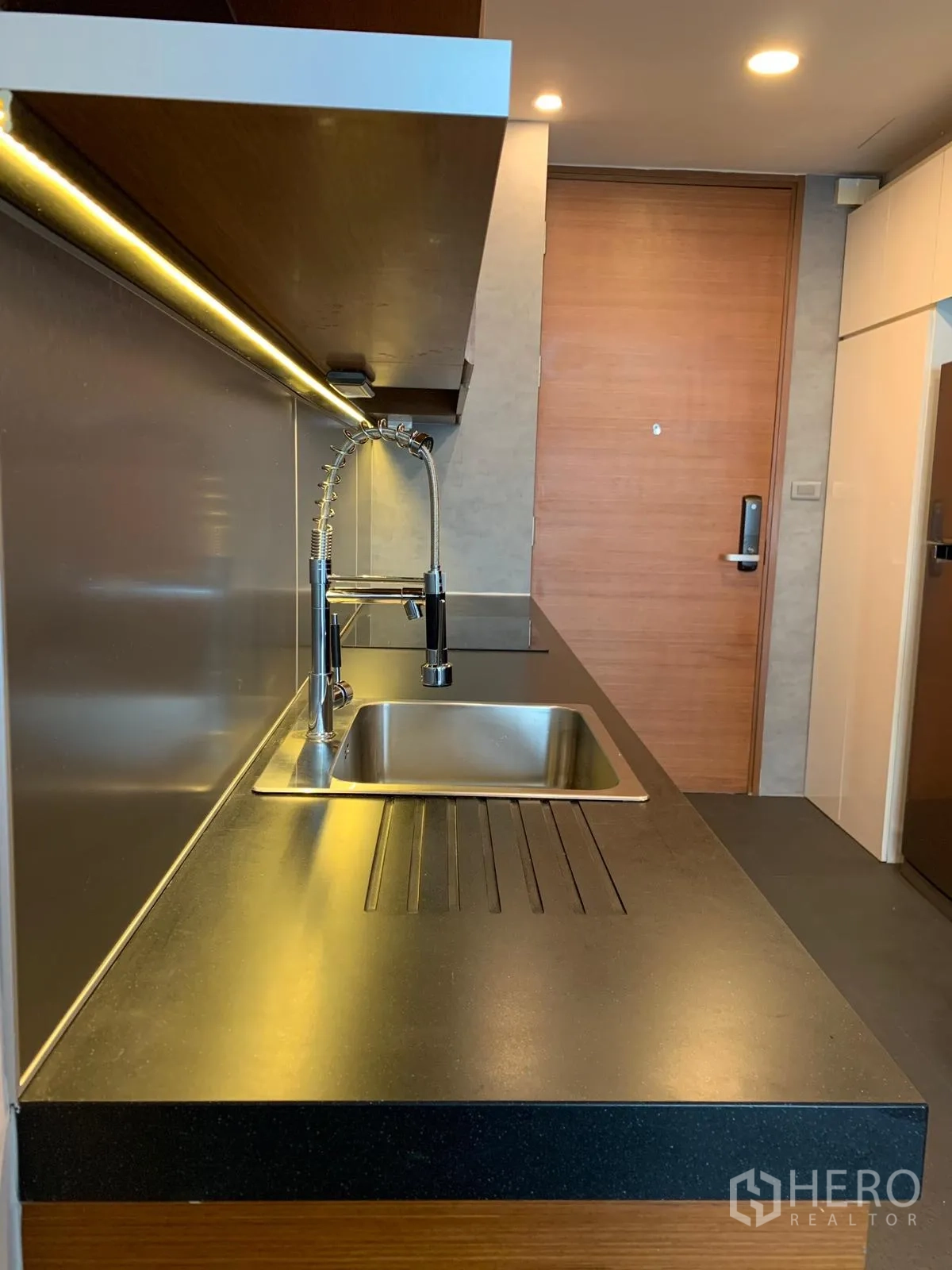 公寓 出售在Khlong Toei, Bangkok - 厨房工作台与水槽，吊柜下灯光，靠近入户门。