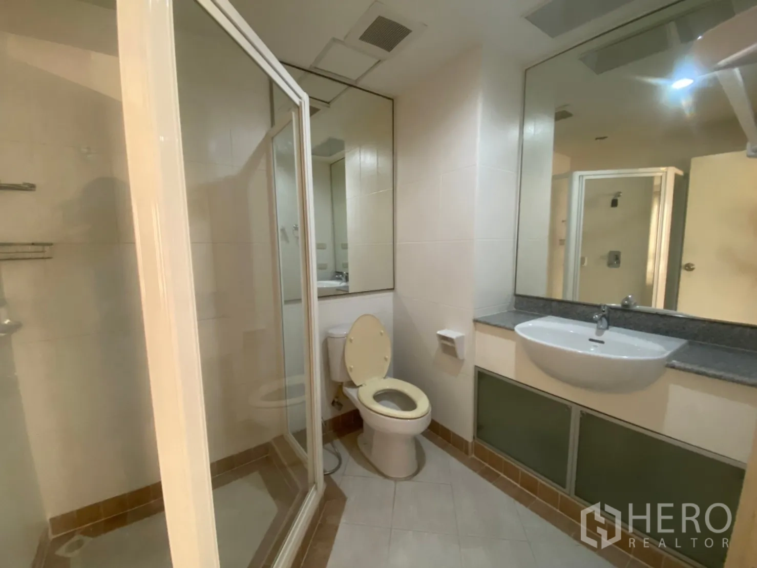 Condominium for rent or sale in Sathon, Bangkok - Bathroom with wide mirror, vanity, toilet and a glass-enclosed shower.