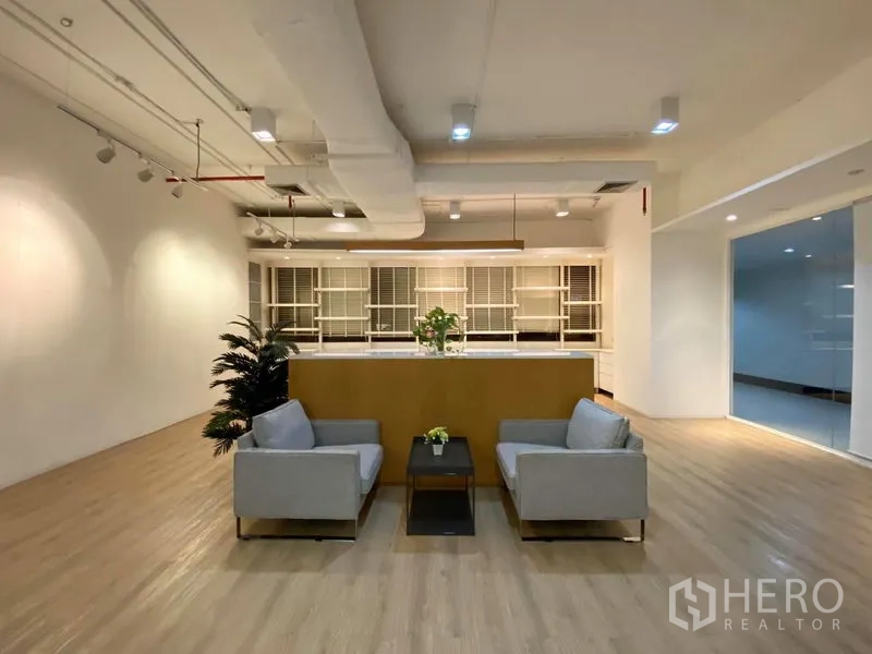 Office Space for rent in Bangkok - Lounge area with two grey sofas, a coffee table, wood floors and a counter with shelving behind.