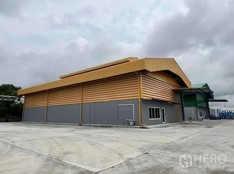 Warehouse for rent in Lat Lum Kaeo, Pathum Thani - Side view of steel warehouse with expansive driveway and perimeter wall.