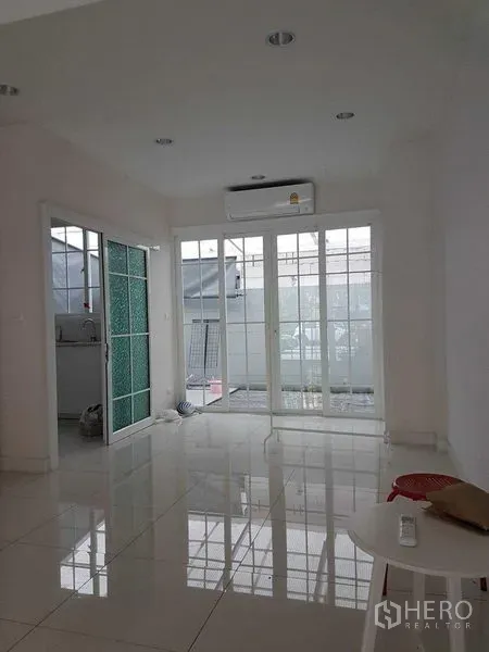 联排别墅 出租在Bang Na, Bangkok - 一楼明亮空间，白色地砖，推拉落地门与空调，通向前庭露台。
