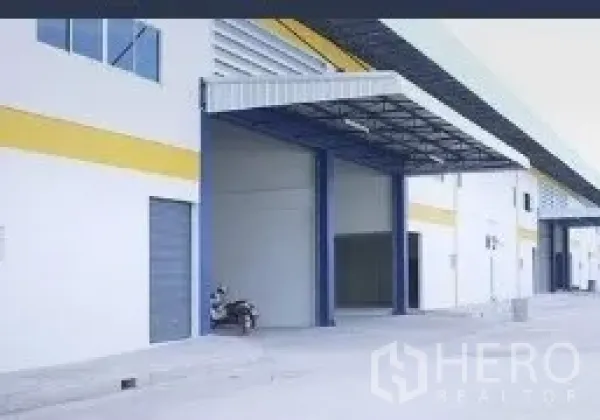 工厂 出租在Mueang Samut Sakhon, Samut Sakhon - 工业仓库外立面，宽电动卷闸门、带顶装卸区与人行门，车道宽敞。