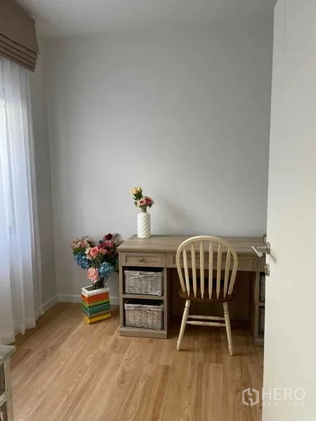 Townhouse for rent in Samut Prakan - Study nook with wooden desk, chair, wicker drawers and decorative flowers near a window.