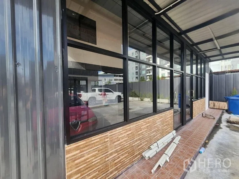 Warehouse for rent in Suan Luang, Bangkok - Side walkway under a canopy with glass windows and mid-rise buildings behind.