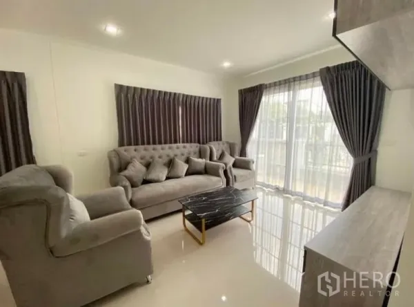 Detached House for rent or sale - Bright living room with grey tufted sofa set, marble coffee table and wide glazing with curtains.