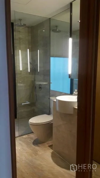 Condominium for sale in Sathon, Bangkok - Modern bathroom with glass-enclosed shower, toilet and vertical vanity lighting.