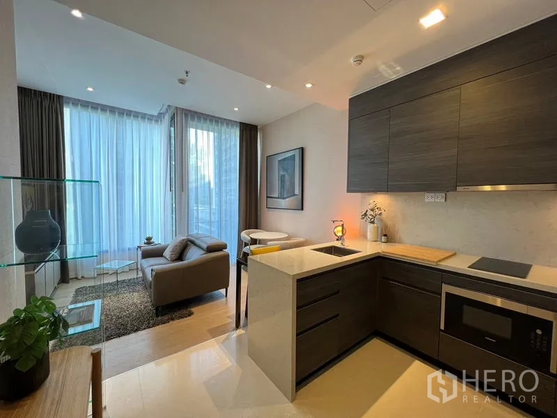 Condominium for rent in Watthana, Bangkok - Open-plan kitchen with dark cabinetry and quartz countertops facing a light-filled living area.