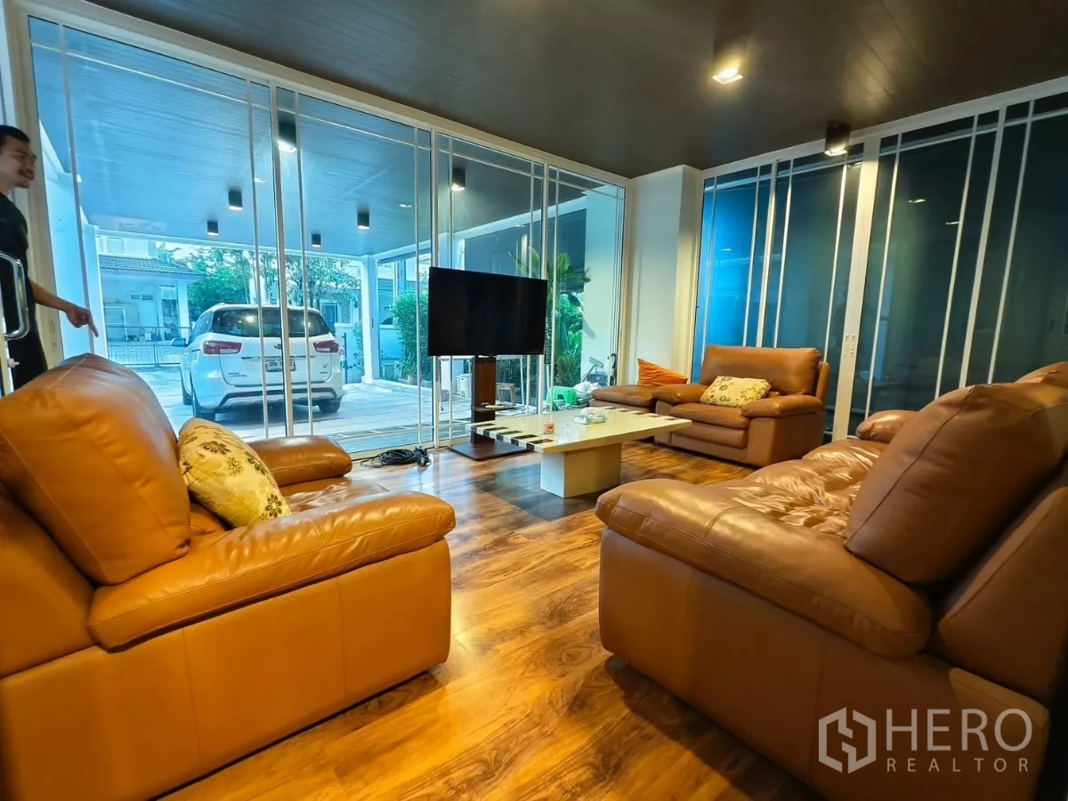 Detached House for rent in Bang Kapi, Bangkok - Living room with leather sofas, TV and floor‑to‑ceiling sliding glass to carport.
