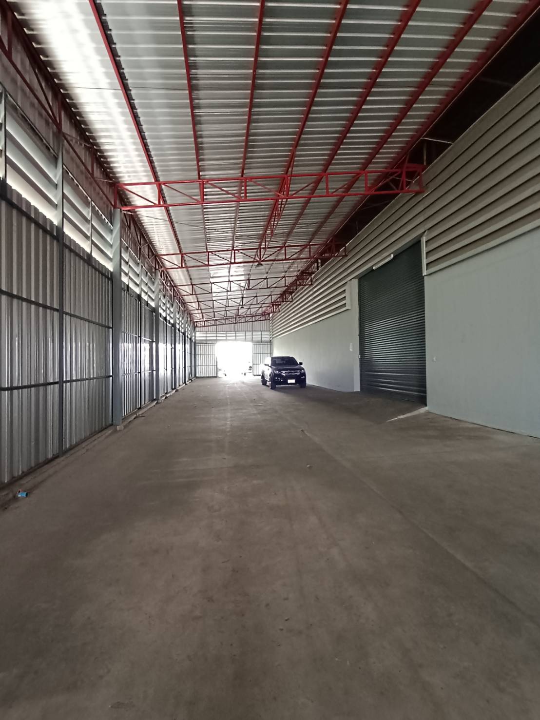 Warehouse for rent in Lat Krabang, Bangkok - Covered loading corridor with steel roof, red trusses and roller shutters for truck access.