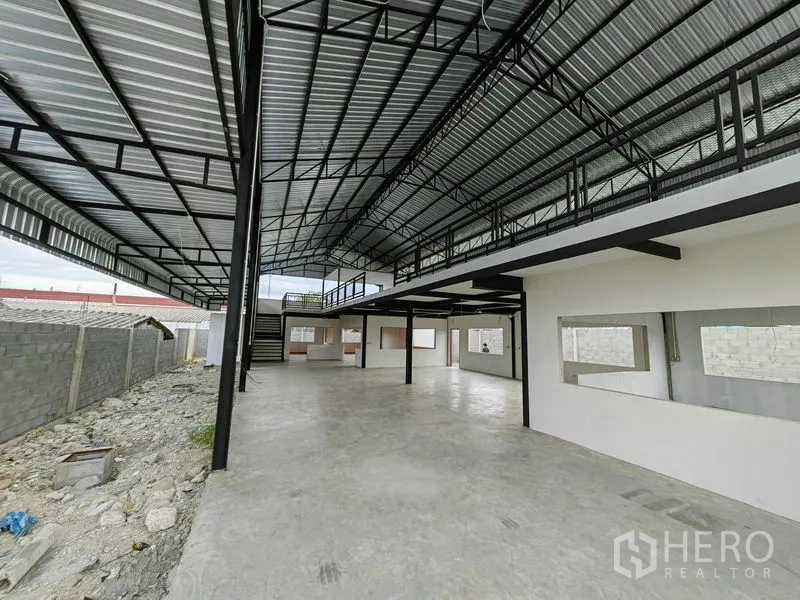 Factory for rent or sale in Mueang Samut Prakan, Samut Prakan - Wide-span production hall under corrugated roof with long mezzanine and concrete floor.