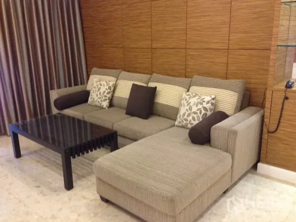 Condominium for rent in Khlong Toei, Bangkok - L-shaped sofa with patterned cushions beside a wooden feature wall and a dark coffee table.