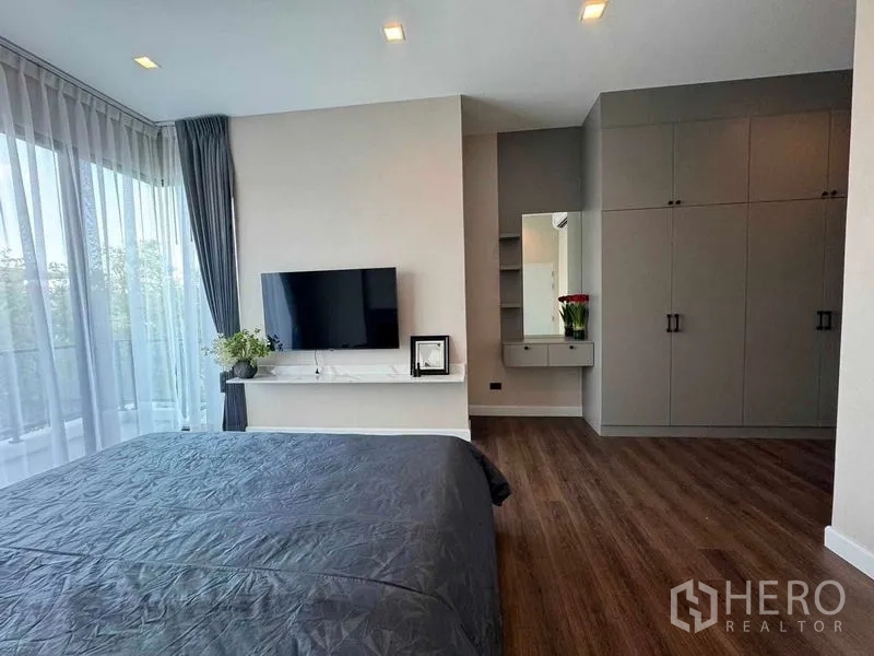 Detached House for rent or sale in Bang Phli, Samut Prakan - Master bedroom with floor-to-ceiling curtains, wall-mounted TV, built-in wardrobes and wood floors.