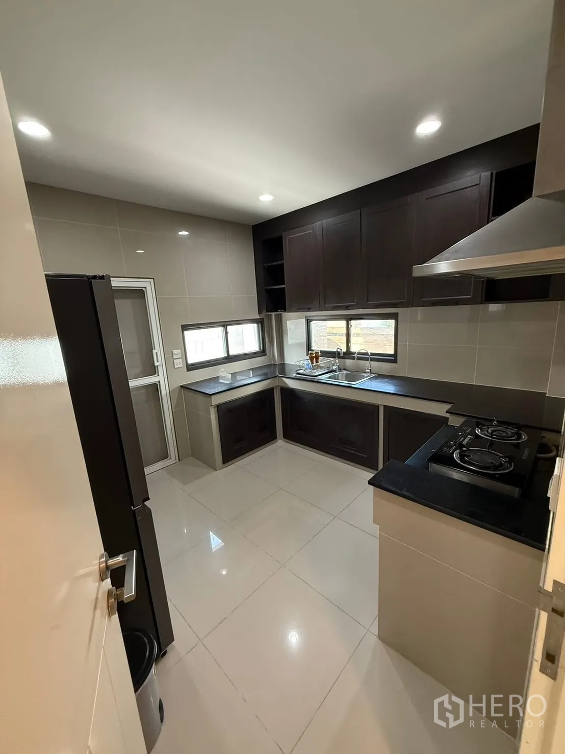 Detached House for rent in Prawet, Bangkok - Bright tiled kitchen with refrigerator space, corner sink beneath windows, and ample overhead storage.