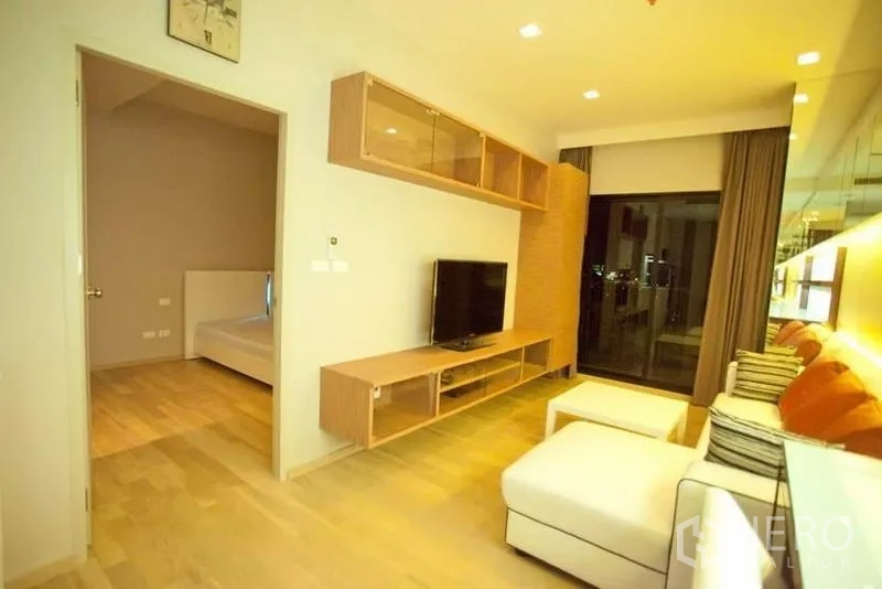 Condominium for rent or sale in Watthana, Bangkok - Bright living room with L-shaped sofa, TV console, wood floors and balcony view with the bedroom door open.