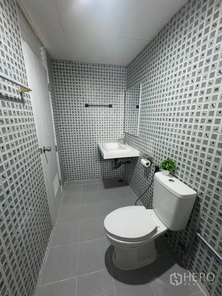 Condominium for rent in Huai Khwang, Bangkok - Bathroom with patterned tile walls, toilet, wall-mounted sink, mirror and grey floor tiles.