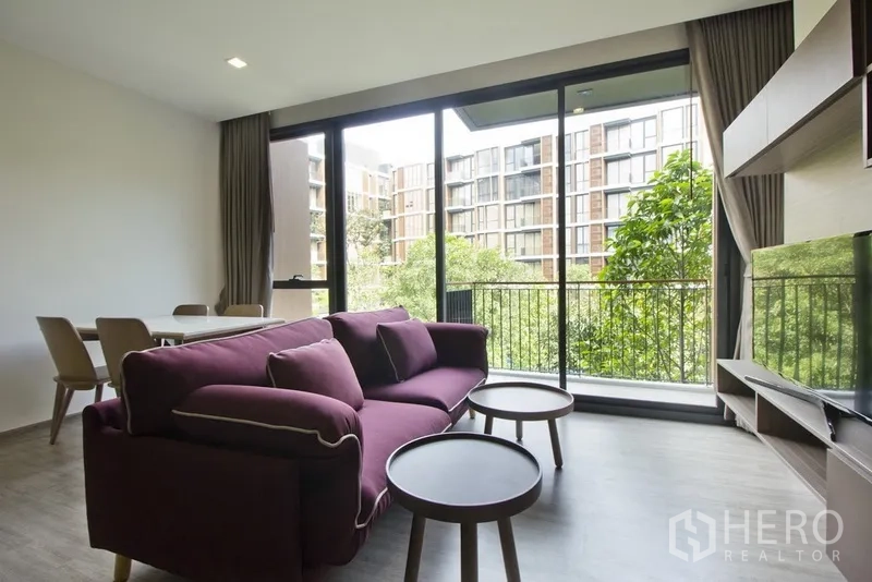 คอนโด ให้เช่าในWatthana, Bangkok - ห้องนั่งเล่นพร้อมโซฟาโต๊ะกลางทรงกลมและระเบียงมองเห็นต้นไม้และอาคารโลว์ไรส์รอบๆ