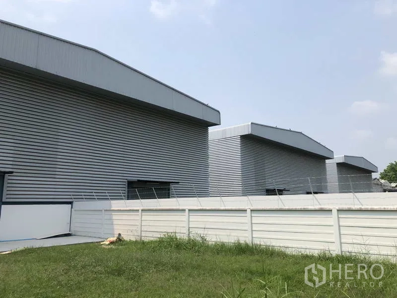 工厂 出售在Sai Noi, Nonthaburi - 多栋现代厂房成排分布，白色围墙与草地相隔。
