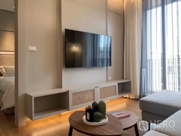 Condominium for rent or sale in Watthana, Bangkok - Living room with wall-mounted TV, media console and floor-to-ceiling curtains.