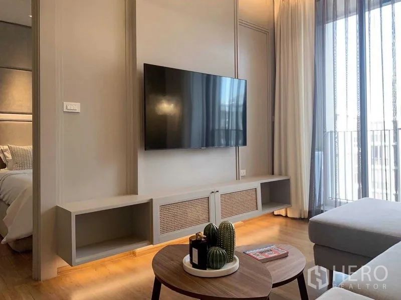 Condominium for rent or sale in Watthana, Bangkok - Living room with wall-mounted TV, media console and floor-to-ceiling curtains.