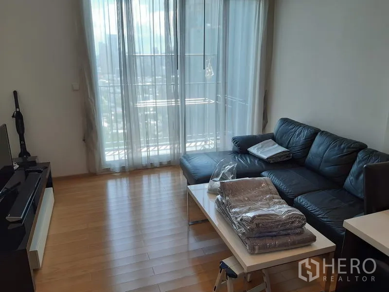 คอนโด ให้เช่าในKhlong Toei, Bangkok - ห้องนั่งเล่นสว่าง โซฟาหนัง ชั้นวางทีวี และประตูกระจกสูงจรดเพดานออกระเบียง