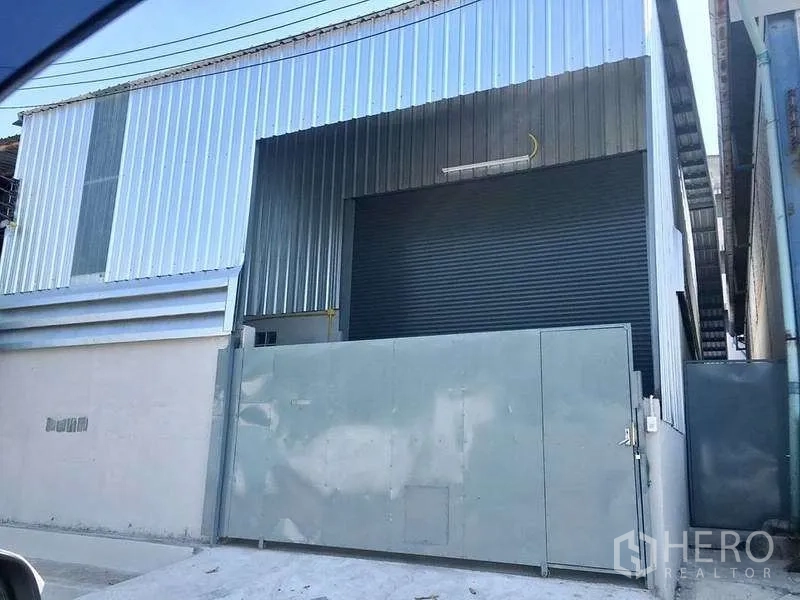 Warehouse for rent in Mueang Samut Prakan, Samut Prakan - Metal-clad warehouse exterior with large roller shutter and secure sliding gate.