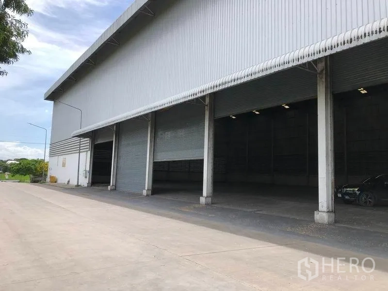 货栈 出租在Phra Nakhon Si Ayutthaya - 多扇卷闸门与有顶装卸区，旁为混凝土硬地。