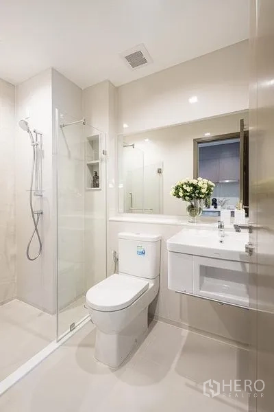 Condominium for sale in Chatuchak, Bangkok - Bright contemporary bathroom with glass shower enclosure, vanity, and toilet.