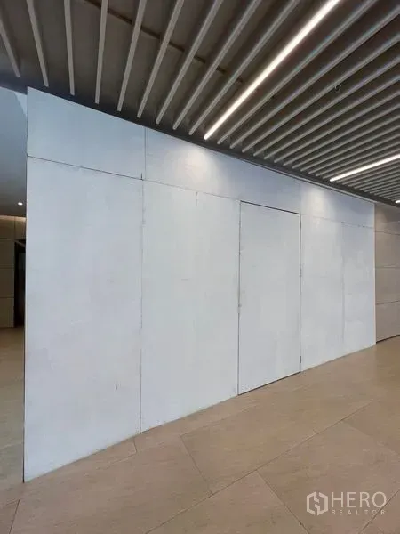 零售空间 出租在Pathum Wan, Bangkok - 现代走廊内白色临时围挡的商铺立面，顶部为格栅吊顶。