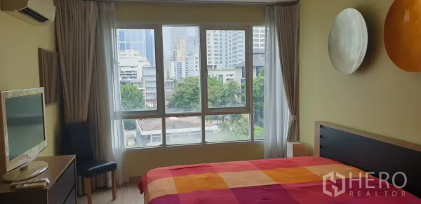 คอนโด ให้เช่าในKhlong Toei, Bangkok - ห้องนอนสว่างพร้อมหน้าต่างบานใหญ่ วิวตึกเมือง และผ้าปูที่นอนสีสันสดใส