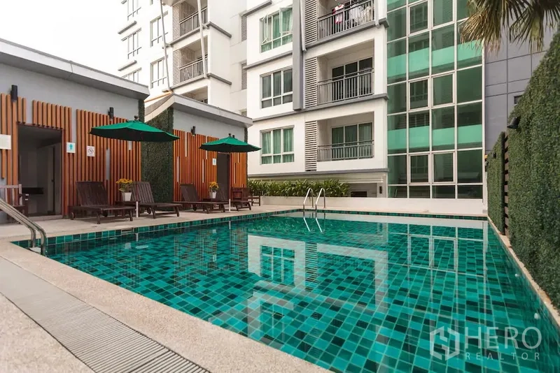 公寓 出租在Khlong Toei, Bangkok - 公寓户外泳池，设躺椅和遮阳伞，临近楼栋立面。