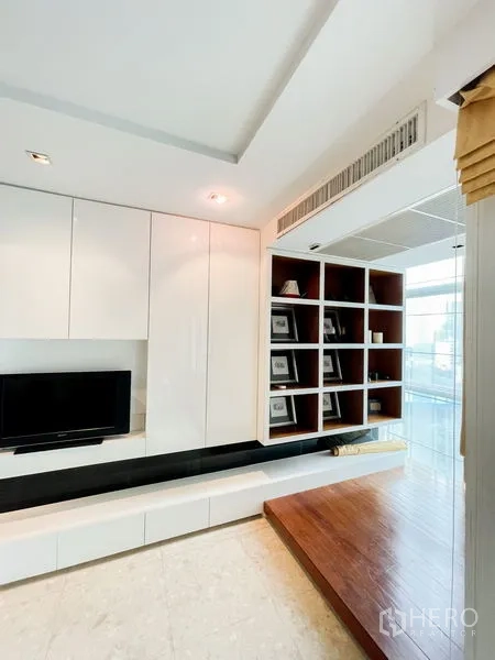 Condominium for rent in Khlong Luang, Pathum Thani - Built-in white TV wall with open shelving and a wood platform beside a floor-to-ceiling window.