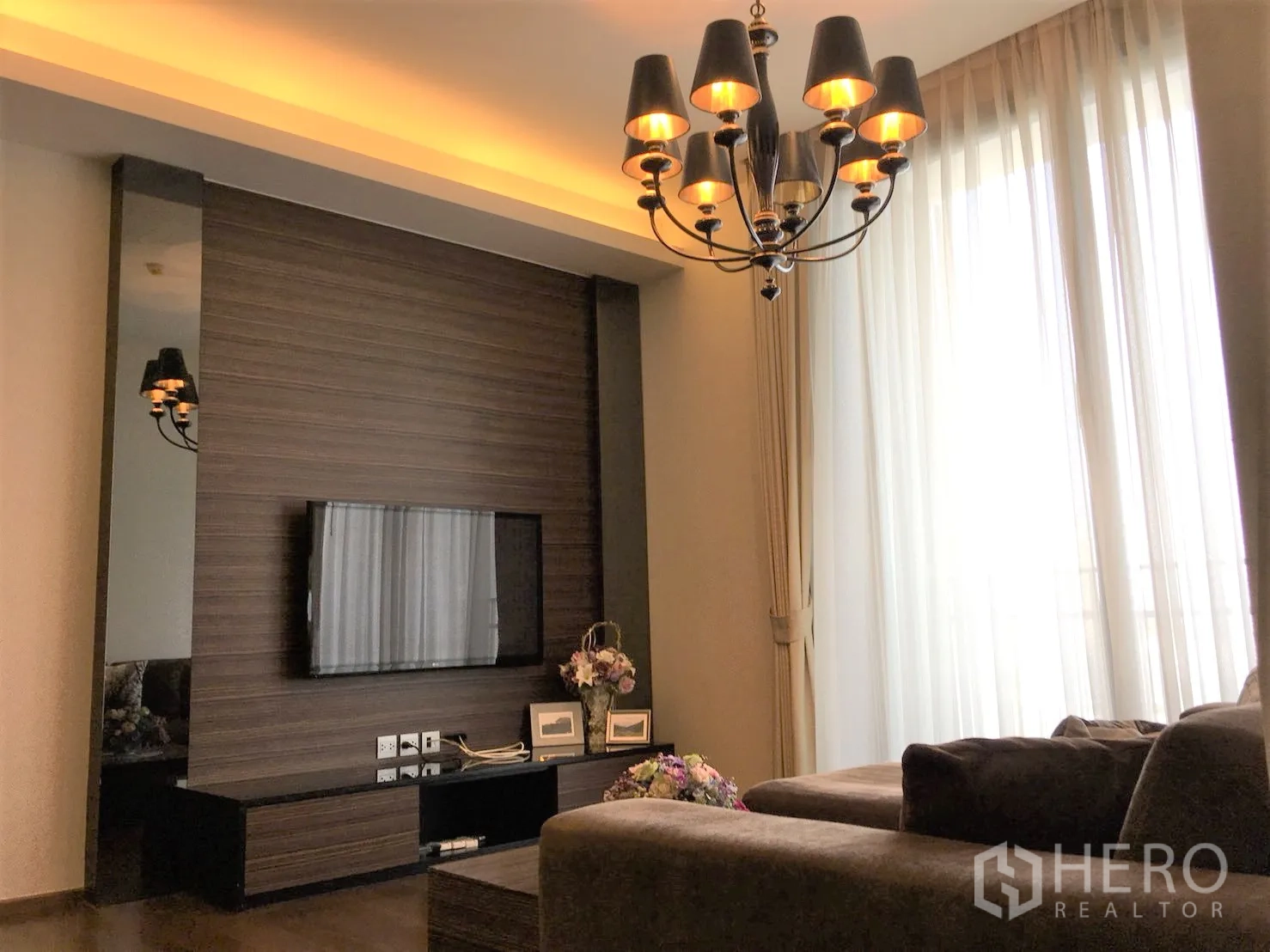 คอนโด ให้เช่าในWatthana, Bangkok - ห้องนั่งเล่นผนังทีวีลายไม้ โซฟาตัวแอล และไฟซ่อนเพดานโทนอุ่น