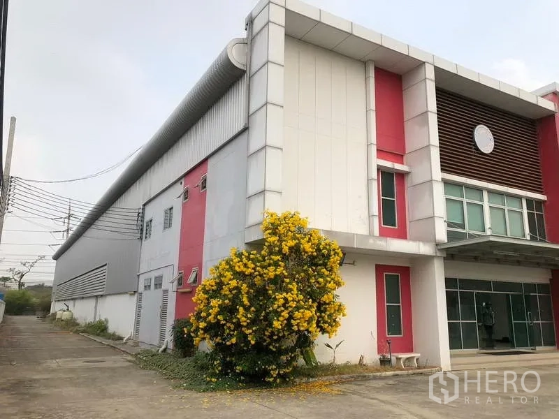 工厂 出租在Bang Sao Thong, Samut Prakan - 工厂侧立面，红色立柱与开花灌木景观。