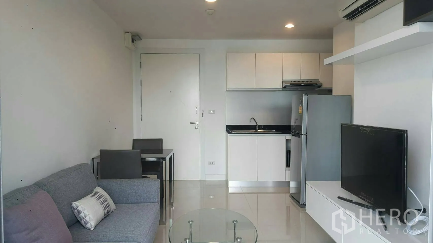 公寓 出租在Phaya Thai, Bangkok - 客厅与双人餐桌全景，入户门旁为简洁白色厨房柜体。